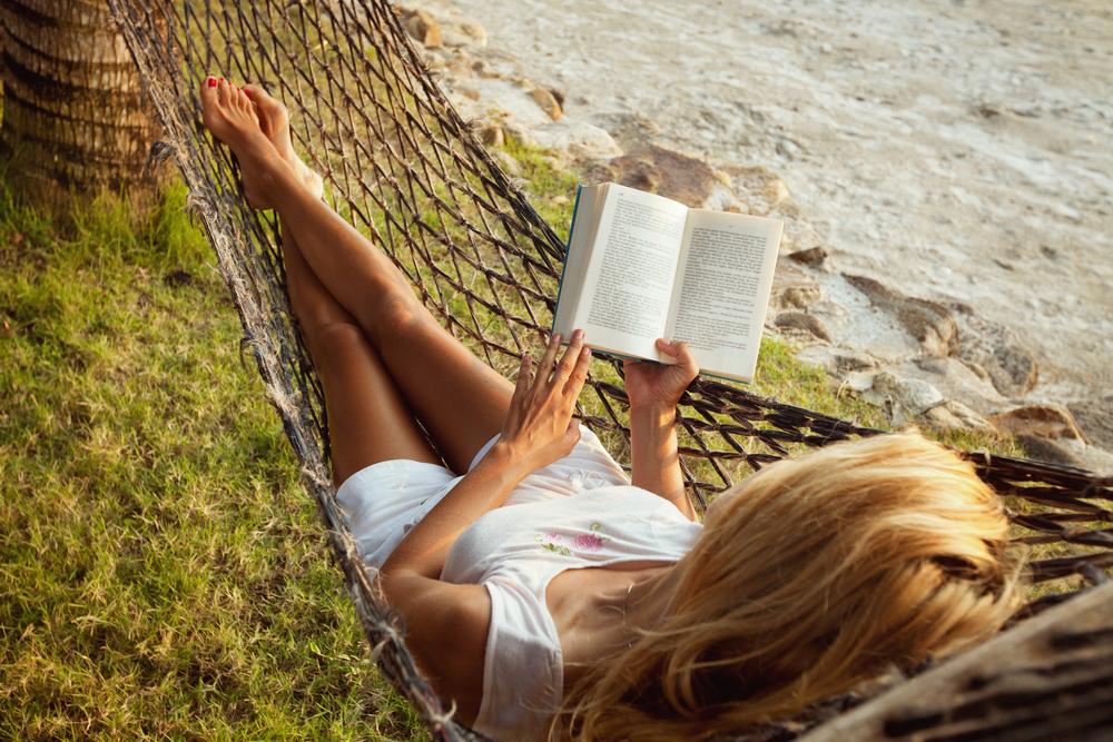 Woman reads book in hammock on beach