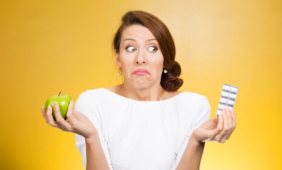 Woman shrugging her shoulders while holding an apple and a pill container
