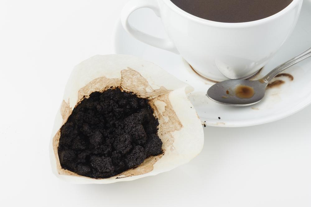 Used coffee grounds beside a cup of coffee