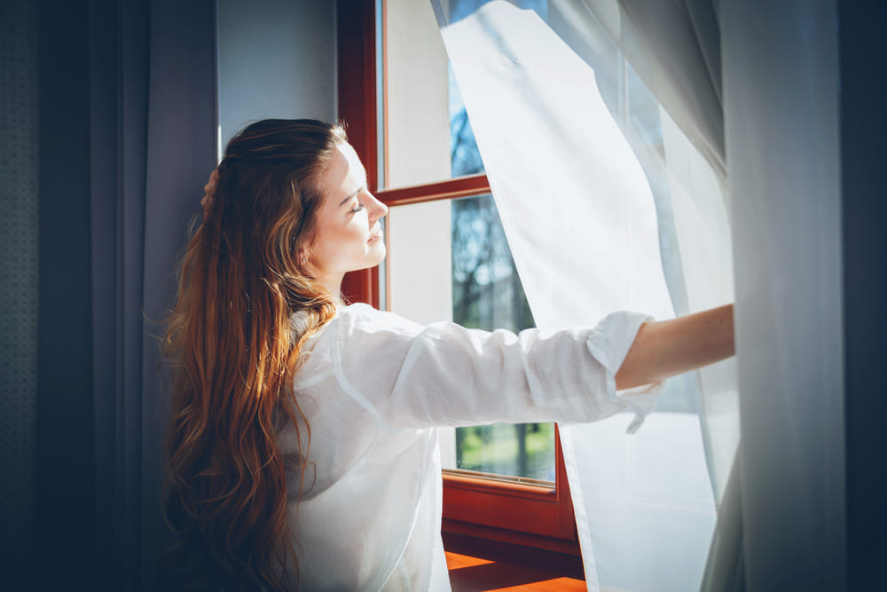 Woman opening curtains to let natural light in
