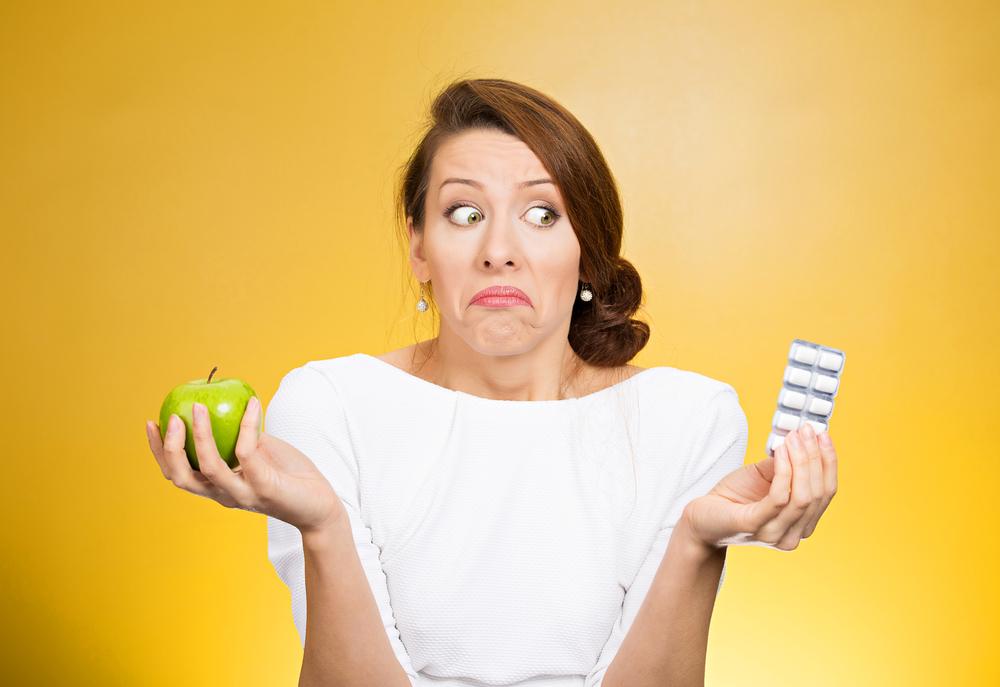 Woman shrugging her shoulders while holding an apple and a pill container